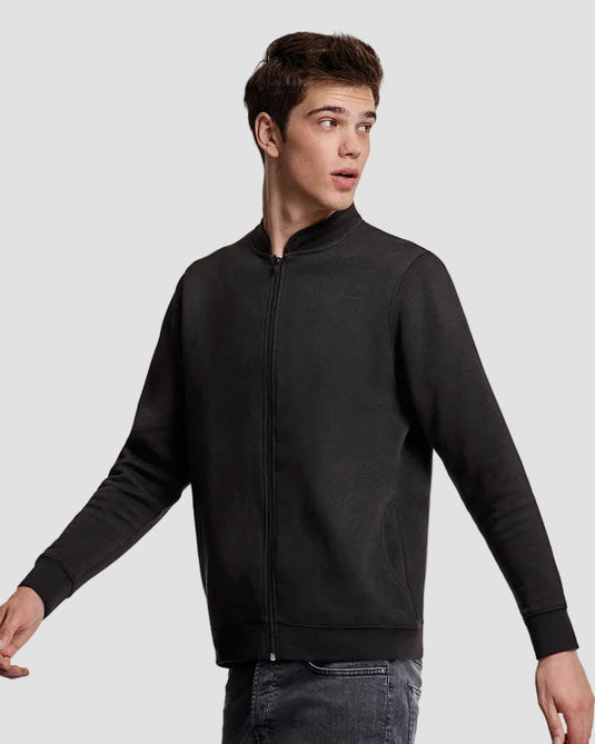 A young man wearing a black zip-up jacket with a stand collar, shown from the waist up against a plain light gray studio background.