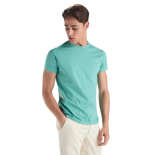 Man wearing a teal t-shirt and white pants on a light gray background