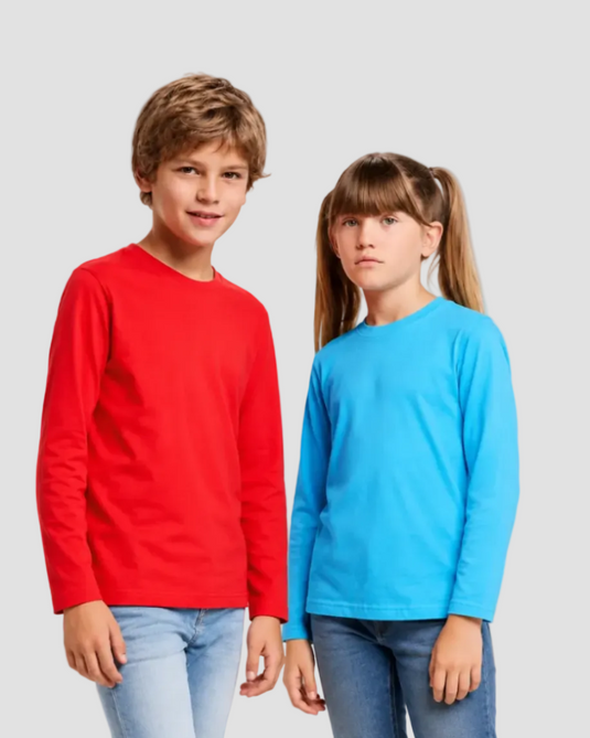 Two children modeling long-sleeve crewneck t-shirts, one in bright red and the other in bright blue, paired with light-wash jeans, against a solid light gray background.