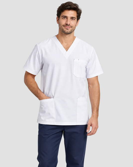 A man wearing a white V-neck scrub top with a chest pocket and two lower front pockets, paired with navy pants, against a light gray studio background.