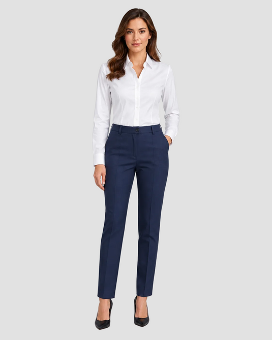 A woman modeling a white long-sleeve button-down shirt and navy blue tailored trousers, paired with black heels, against a solid gray studio background.
