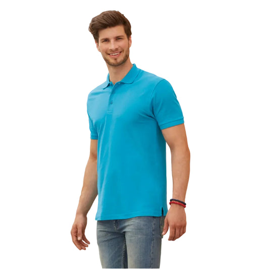 A man wearing a bright turquoise blue short-sleeve polo shirt and blue jeans, standing against a beige stone wall.
