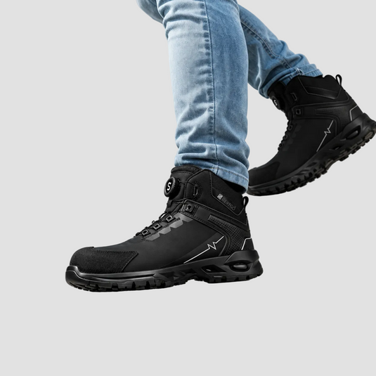 A person wearing black high-top safety boots with light blue jeans, shown from the calves down against a neutral gray studio background.