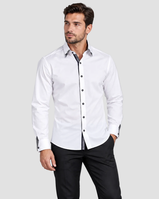 A man wearing a white long-sleeve button-down shirt with black trim and black trousers, standing against a solid gray studio background.