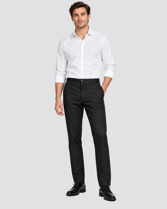 A man modeling a white long-sleeve button-down shirt and black trousers with black dress shoes, standing against a light gray studio background.