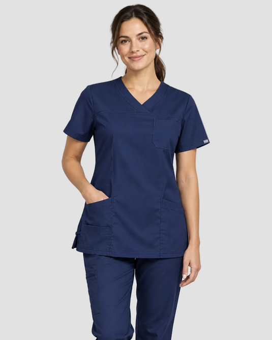 A woman modeling a navy blue scrub top and matching scrub pants against a light gray studio background.