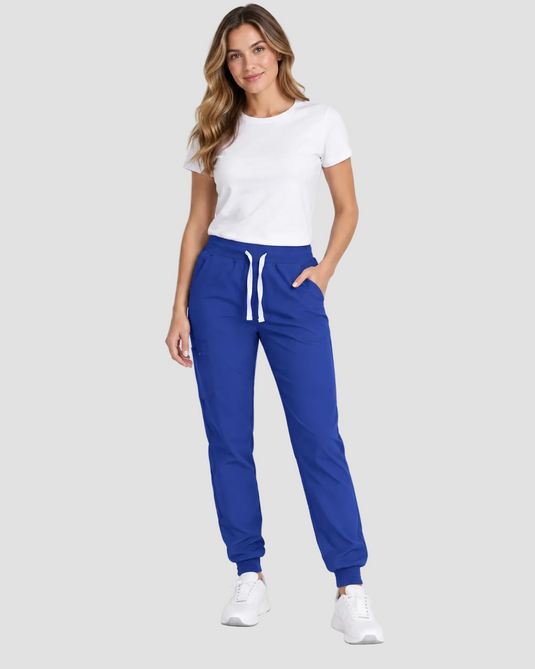 A woman modeling a pair of royal blue jogger sweatpants with a white drawstring, paired with a white t-shirt and white sneakers, against a light gray studio background.